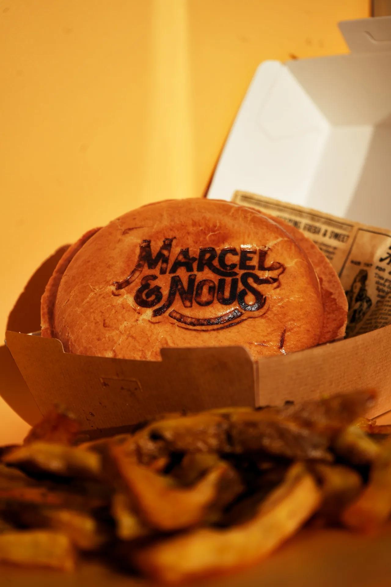Pain à burger marqué au logo Marcel & Nous dans sa boîte